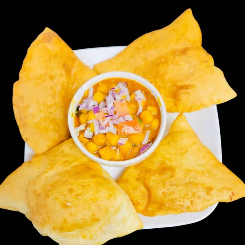 Indian chole bhature, featuring fluffy fried bread surrounding a bowl of chickpea curry topped with onions.