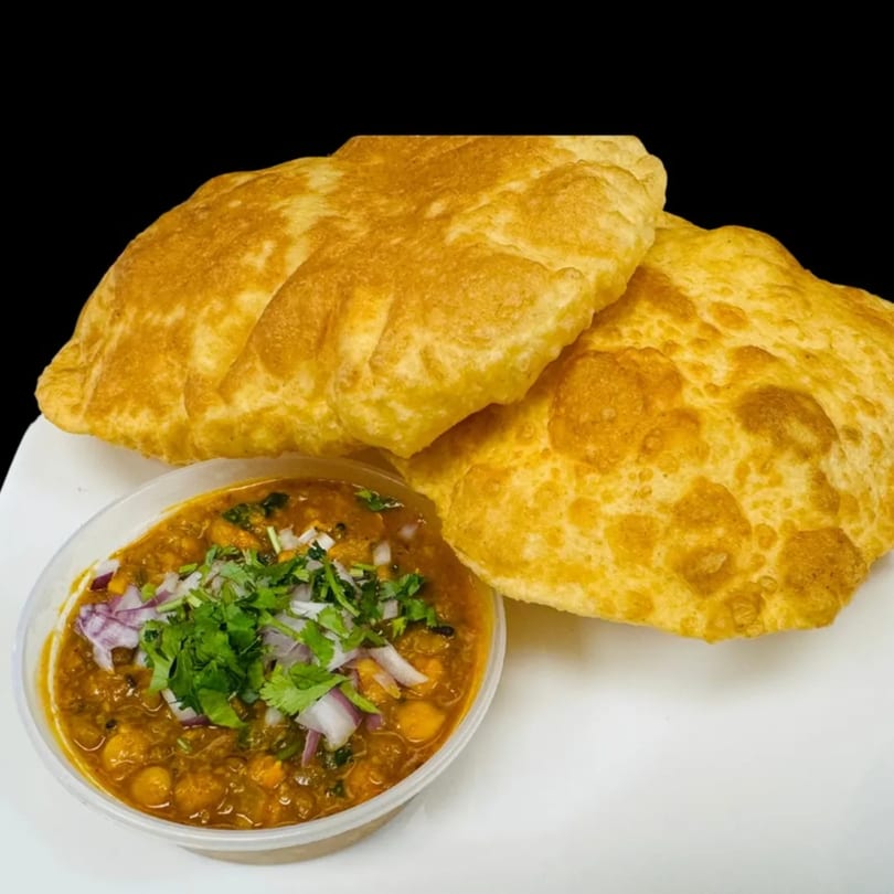 Two golden-brown fried Indian puri breads next to a bowl of chana masala topped with onions and cilantro.