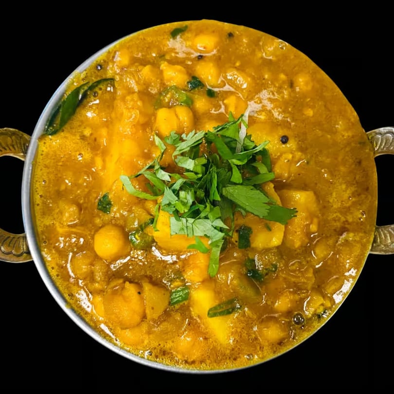 Close-up of a vibrant yellow Indian chickpea and potato curry, garnished with fresh cilantro in a metal bowl.