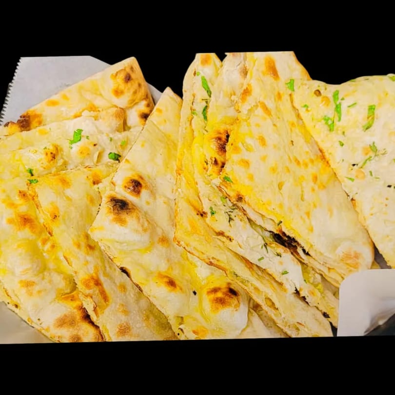 Close-up of a basket filled with golden-brown Indian naan bread, garnished with fresh green herbs.