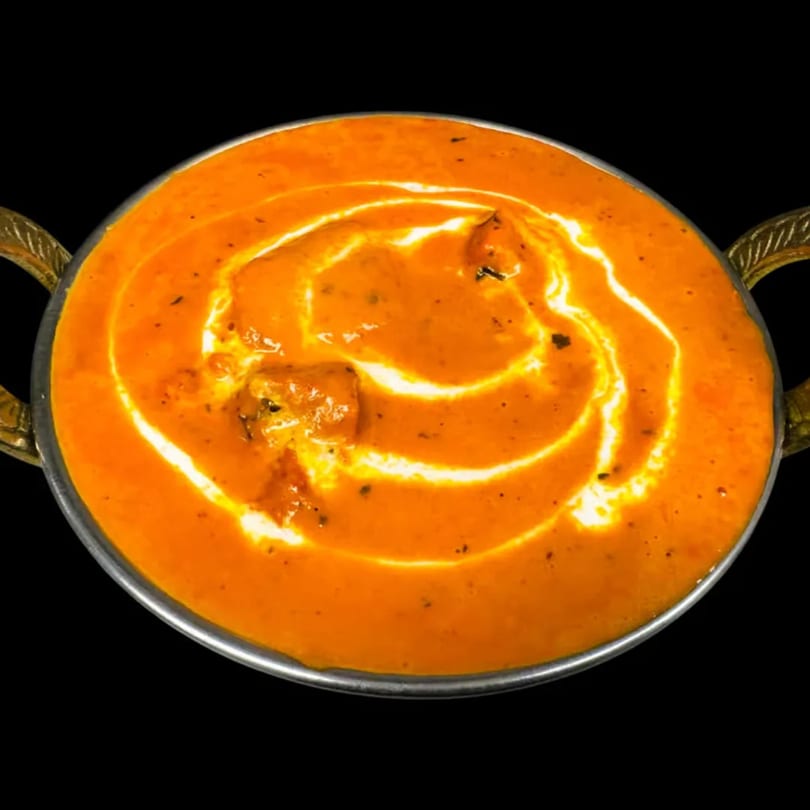 A close-up of a vibrant orange Indian curry with a swirl of cream in a metal bowl.